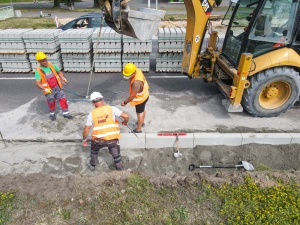 Pracownicy układający krawężnik przy pomocy ciężkiego sprzętu